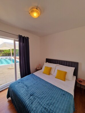 A hotel room with a bed, a nightstand, a window with curtains, and a view of an outdoor swimming pool. - Holiday Home Nino With Private Pool (Split)