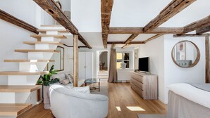 Un salon moderne avec un escalier, des poutres en bois, un téléviseur à écran plat et un grand miroir rond.