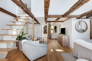 En modern inredning med synliga träbjälkar, en trappa, en vit soffa, en tv och en rund spegel.