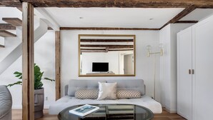 Un salon moderne avec une table basse en verre, un canapé gris, un escalier en bois et une armoire blanche.