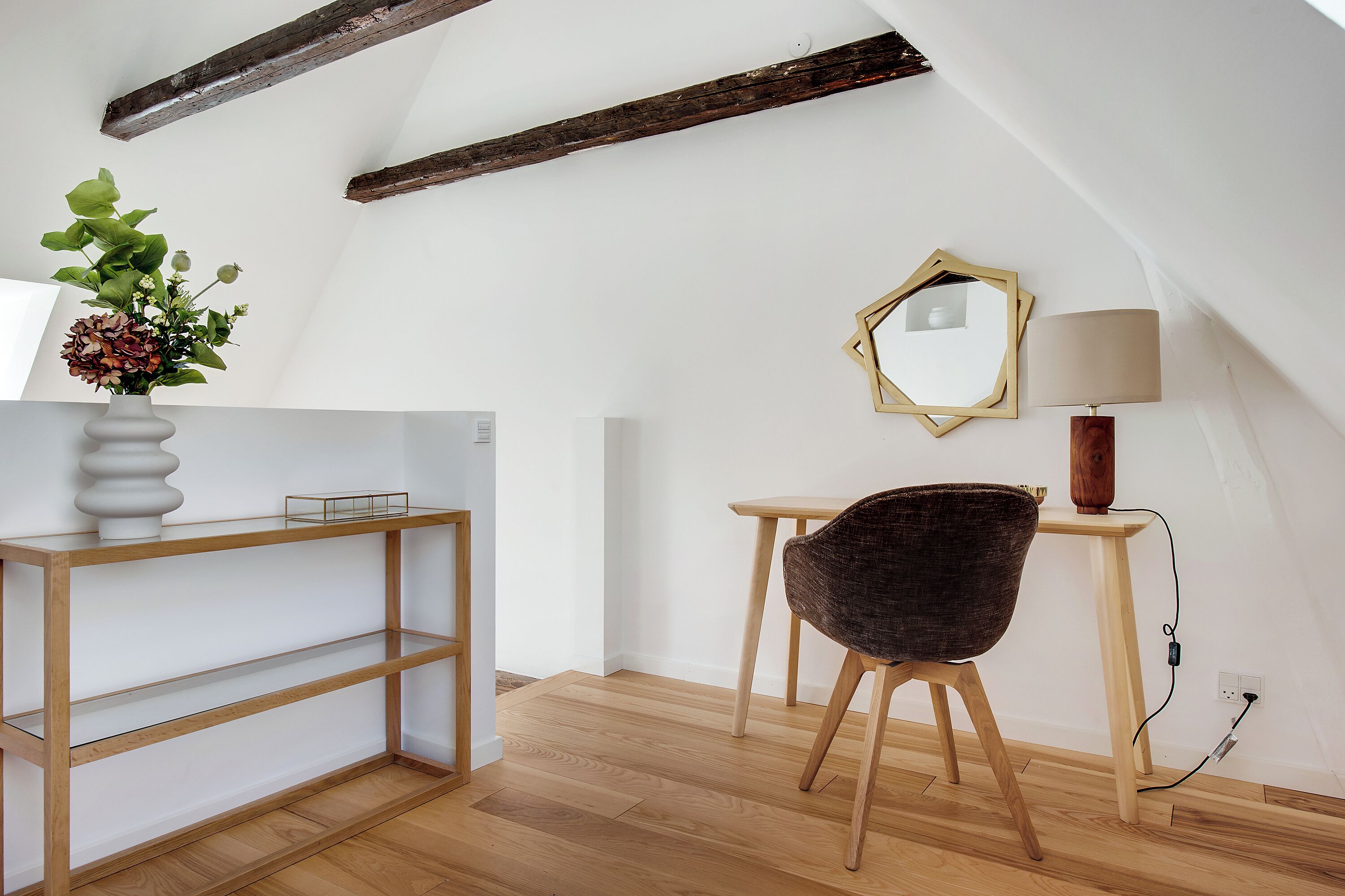 Een kamer met een houten console, een stoel, een lamp en een spiegel aan de muur.