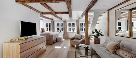 A modern living room with exposed wooden beams, a large flat-screen TV, a sofa, a coffee table, and a potted plant.