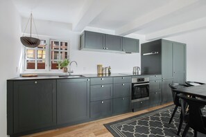 A modern kitchen with dark cabinetry, a built-in oven, and a dining area with a table and chairs.