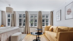 A modern hotel room with a bed, a sofa, a round table, and large windows with curtains. - Regent 2- Endearing 1-bdr Apt in Centre of Copenhagen (Copenhagen)