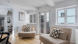 A modern living room with a sofa and armchair, a dining area with a table and chairs, and a view of the outside through large windows. - Regent 2- Endearing 1-bdr Apt in Centre of Copenhagen (Copenhagen)