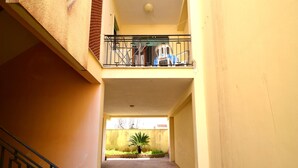 Ein schmaler Korridor mit einem Balkon zur rechten Seite, einer Treppe zur linken Seite und einem kleinen Garten am Ende.