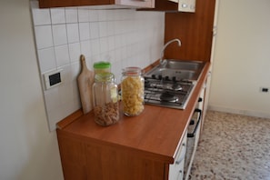 A kitchen with a wooden countertop, a gas stove, and two jars of pasta.