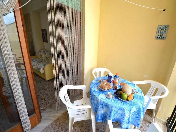 Un coin repas avec une table dressée pour deux personnes, agrémentée d’une nappe bleue et de chaises blanches. Une assiette de fruits, une bouteille d’eau et une tasse sont posés sur la table.