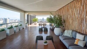 Un espace de détente moderne comprenant un canapé, des fauteuils et une table basse, avec une vue sur la ville grâce à de grandes fenêtres.
