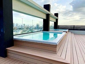 Une piscine à débordement située sur le toit, offrant une vue sur la ville, avec une terrasse en bois et une architecture moderne.
