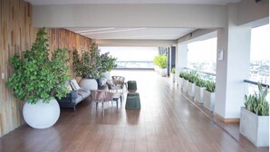 Un balcon spacieux doté d’un plancher en bois, d’un coin salon avec un canapé et des fauteuils, et de plantes en pot.