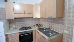 Een kleine keuken met houten kastjes, een gasfornuis, een oven, een spoelbak en een betegelde spatwand.