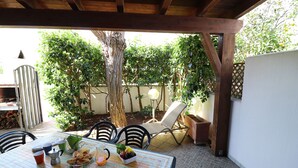 Een overdekt terras met een ontbijttafel, omringd door stoelen en een lounge stoel.