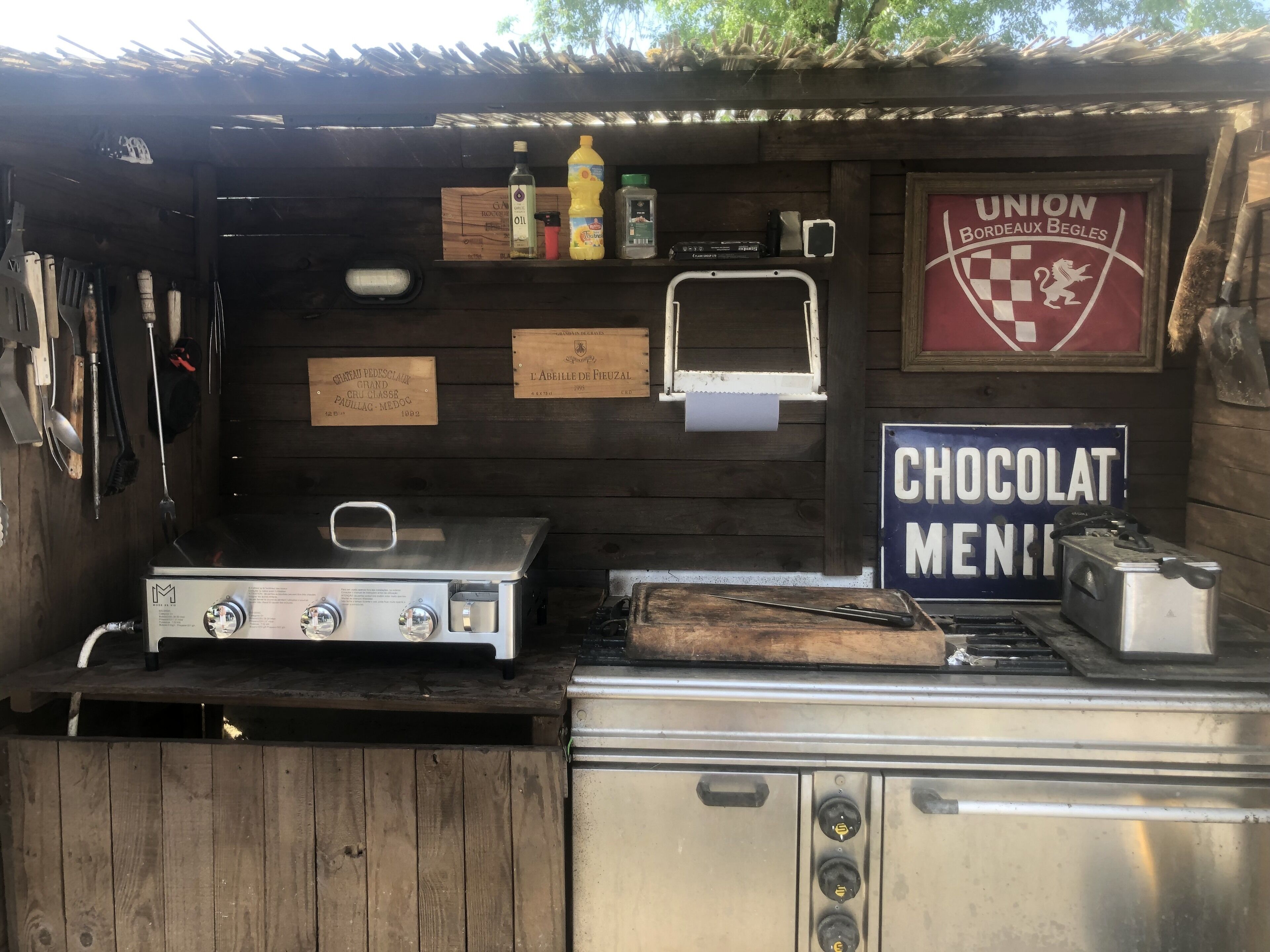 Una cocina rústica al aire libre con estufa a gas, un tostador y un letrero que dice 'CHOCOLAT MENIE'.