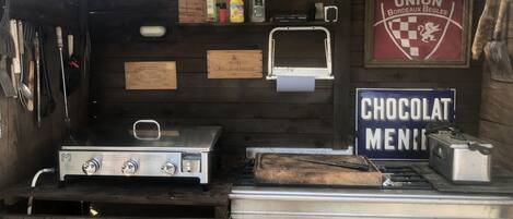 Una cocina rústica al aire libre con estufa a gas, un tostador y un letrero que dice 'CHOCOLAT MENIE'.