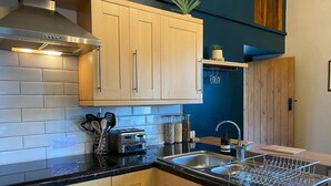 A modern kitchen with light wood cabinets, a stainless steel range hood, a black countertop, and a dish drying rack. - Luxury, Self-contained Country Cottage With View (Scarborough)