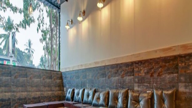 A modern lounge area with a wooden bench and cushioned seating, a glass coffee table, and a stone accent wall. - We Stay - Andheri (Mumbai)