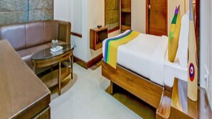 A hotel room with a bed, a sofa, a small table, a TV, and a target decoration. - We Stay - Andheri (Mumbai)