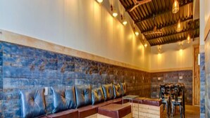 A modern lounge area with wooden benches and cushioned seating, a patterned wall, and a ceiling with exposed beams and hanging lights. - We Stay - Andheri (Mumbai)
