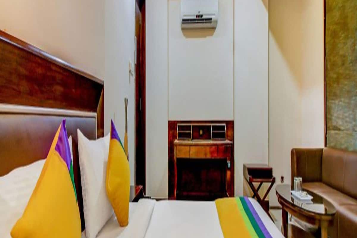 A hotel room with a bed, a sofa, a small table, and an air conditioning unit.