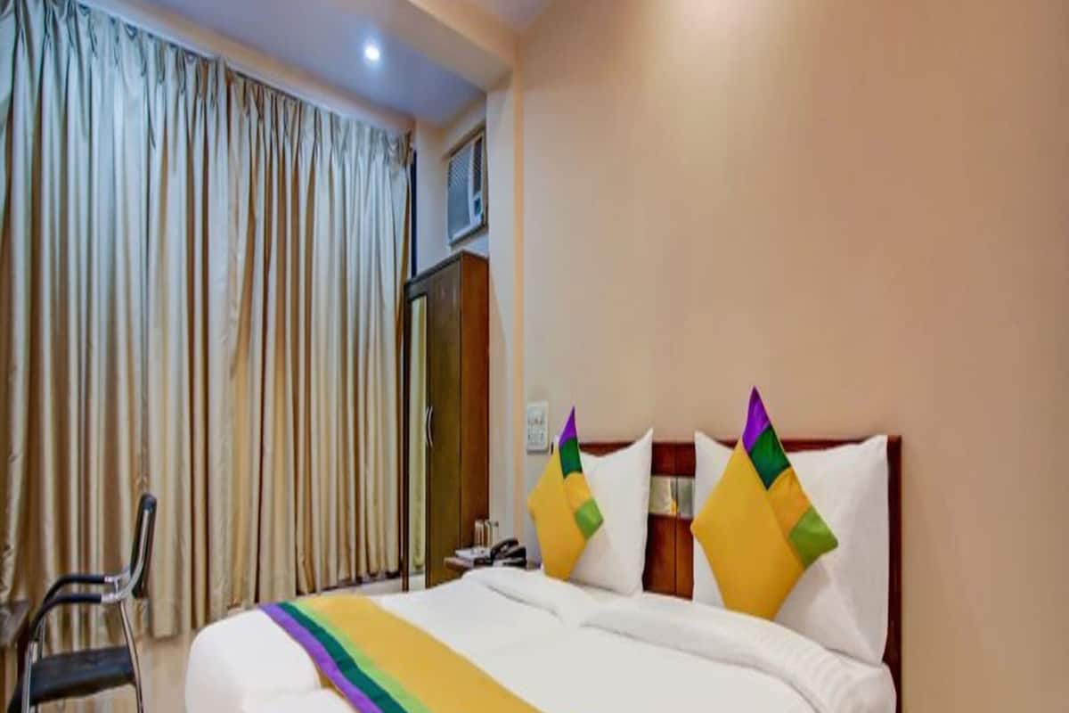 A hotel room with a large bed, a chair, a wardrobe, and a window with curtains.