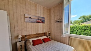 Une chambre avec un mur lambrissé en bois, un lit avec une literie rouge et blanche, une table de chevet avec une lampe et une fenêtre donnant sur un paysage verdoyant.