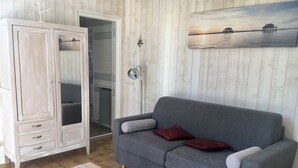Un salon avec un canapé gris, un meuble en bois, une petite table et un tableau représentant un coucher de soleil sur l’eau.