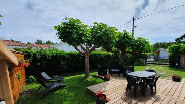 Une terrasse en bois avec une table et des chaises, entourée d’une pelouse bien entretenue et d’un arbre.
