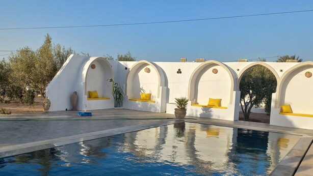A swimming pool with white walls and yellow cushions, surrounded by arched seating areas.