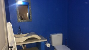 A bathroom with a blue wall, a sink with a mirror, a toilet, and a towel hanging on the wall.