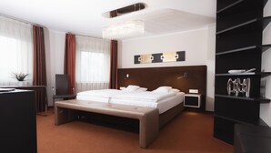 A modern hotel room with a large bed, a bench, a desk, a bookshelf, and a chandelier. - Haus Gerbens (Wickede)