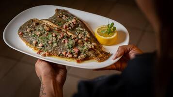 Uma pessoa segurando um prato branco com um filé de peixe coberto com ingredientes picados e uma fatia de limão.