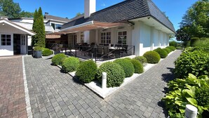 A white building with a black roof, a covered patio area, and a brick pathway. - Haus Gerbens (Wickede)