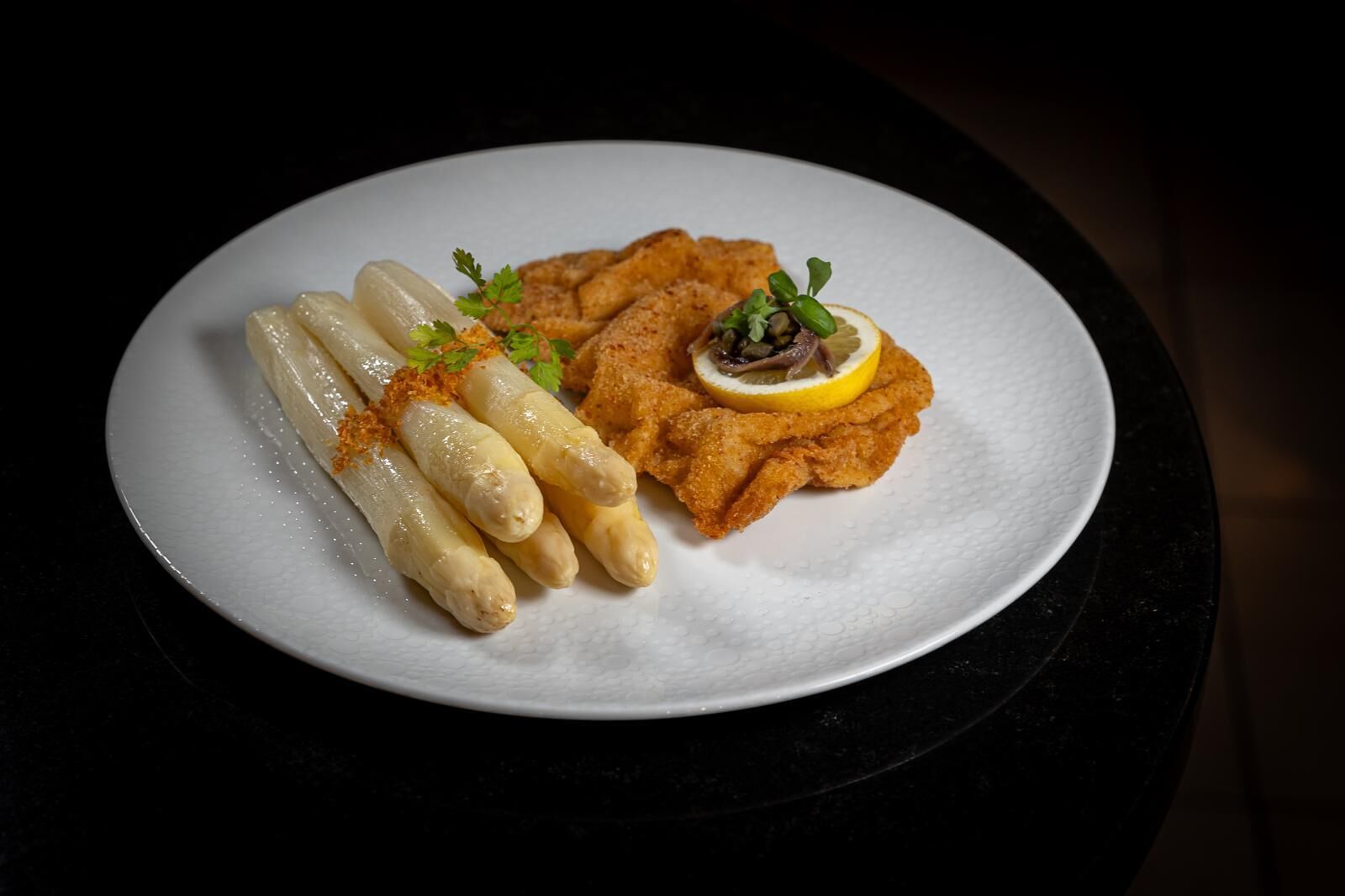 Un plato con milanesa, espárragos y una rodaja de limón.