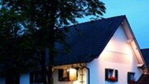 A two-story building with a sloped roof, a small porch, and a visible entrance. - Haus Gerbens (Wickede)