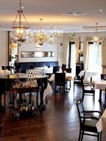 Uma área de refeições com piano, mesas, cadeiras, lustres e um carrinho de bar com garrafas.