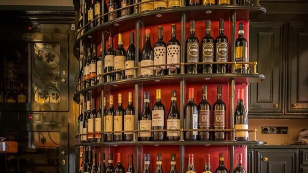 A multi-tiered wine rack with various bottles, set against a dark background with reflective surfaces. - Haus Gerbens (Wickede)