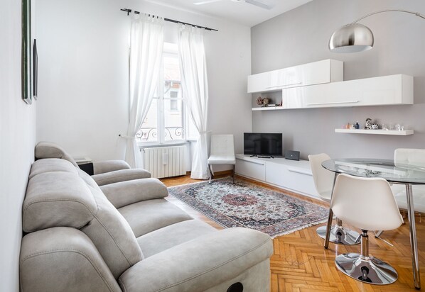 Een moderne woonkamer met een bank, een eettafel met stoelen, een televisie en een decoratief vloerkleed.