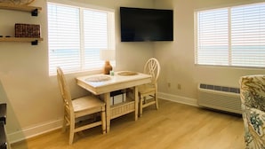 Een eetgedeelte met een tafel en stoelen, een flatscreen televisie aan de wand en een raam met jaloezieën.