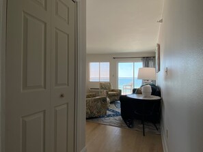 A hotel room with a door, a seating area with two chairs, a table with a lamp, and a view of the ocean through a window. - Beachfront Gulf View Condo by PKRM (Perdido Key)