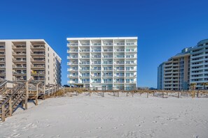 A beachfront hotel with multiple balconies, a sandy beach in front, and a clear blue sky. - Beachfront Gulf View Condo by PKRM (Perdido Key)