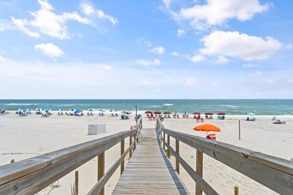 A wooden boardwalk leading to a beach with umbrellas and lounge chairs.