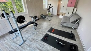 Ein Heimfitnessraum mit einer Langhantelbank, Kurzhanteln, einem Heimtrainer und einer Yogamatte.