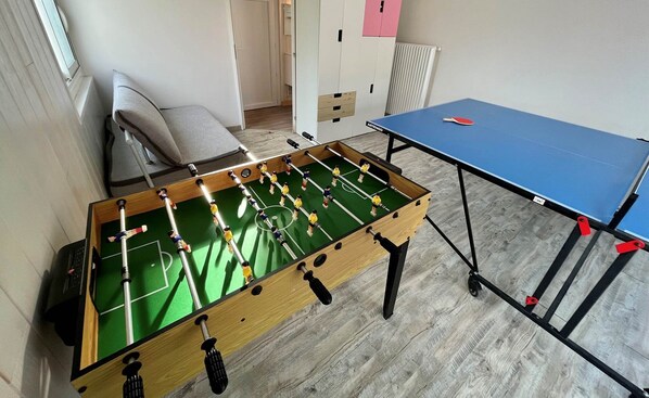 A foosball table and a ping pong table in a room with wooden flooring and a radiator. - Villa (Lanton)