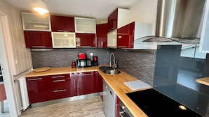 Eine moderne Küche mit roten Schränken, einer Edelstahl-Dunstabzugshaube, einem eingebauten Backofen und einer Holz Arbeitsplatte.