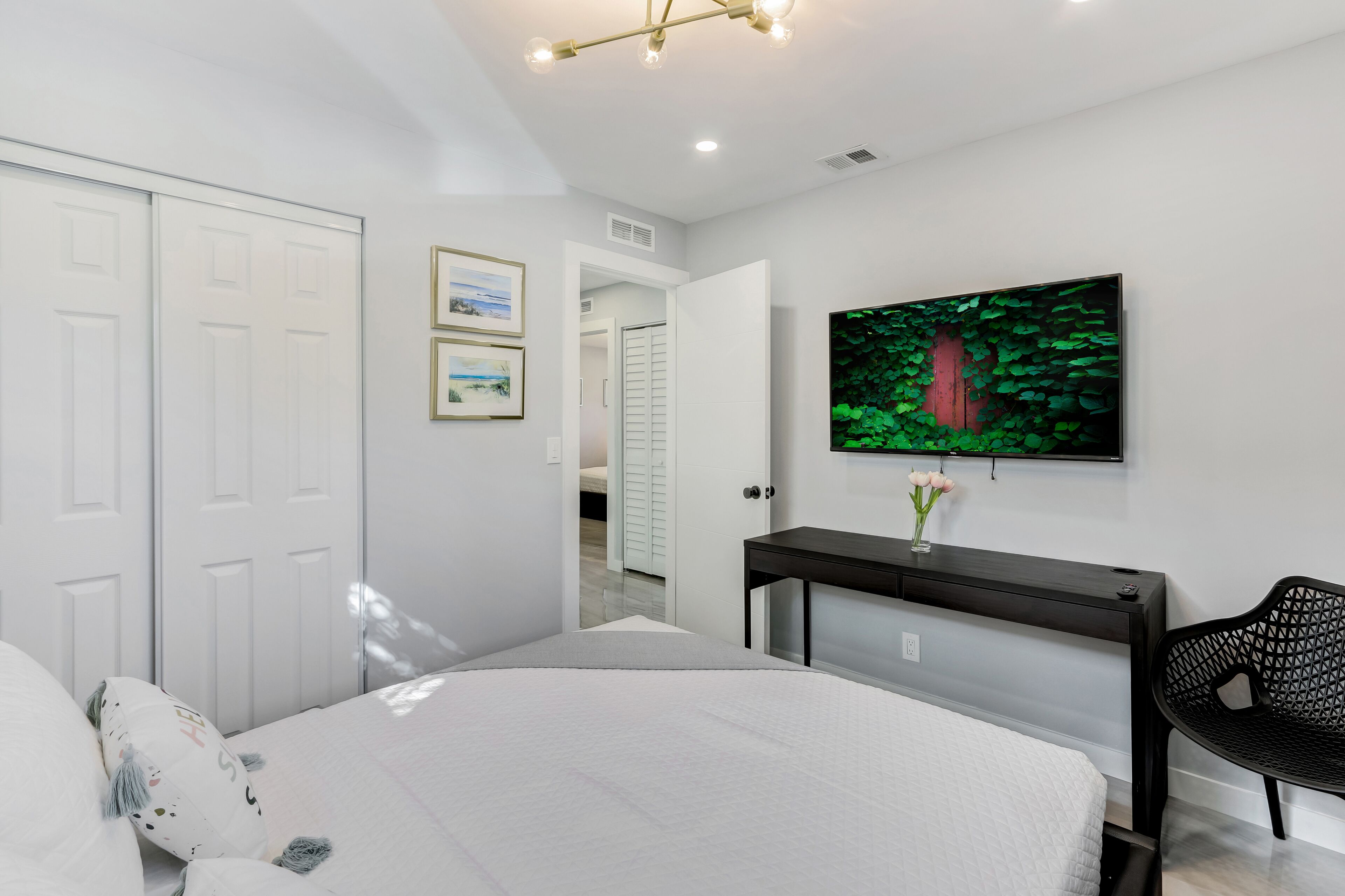 A modern bedroom with a bed, a desk, a chair, and a TV on the wall.