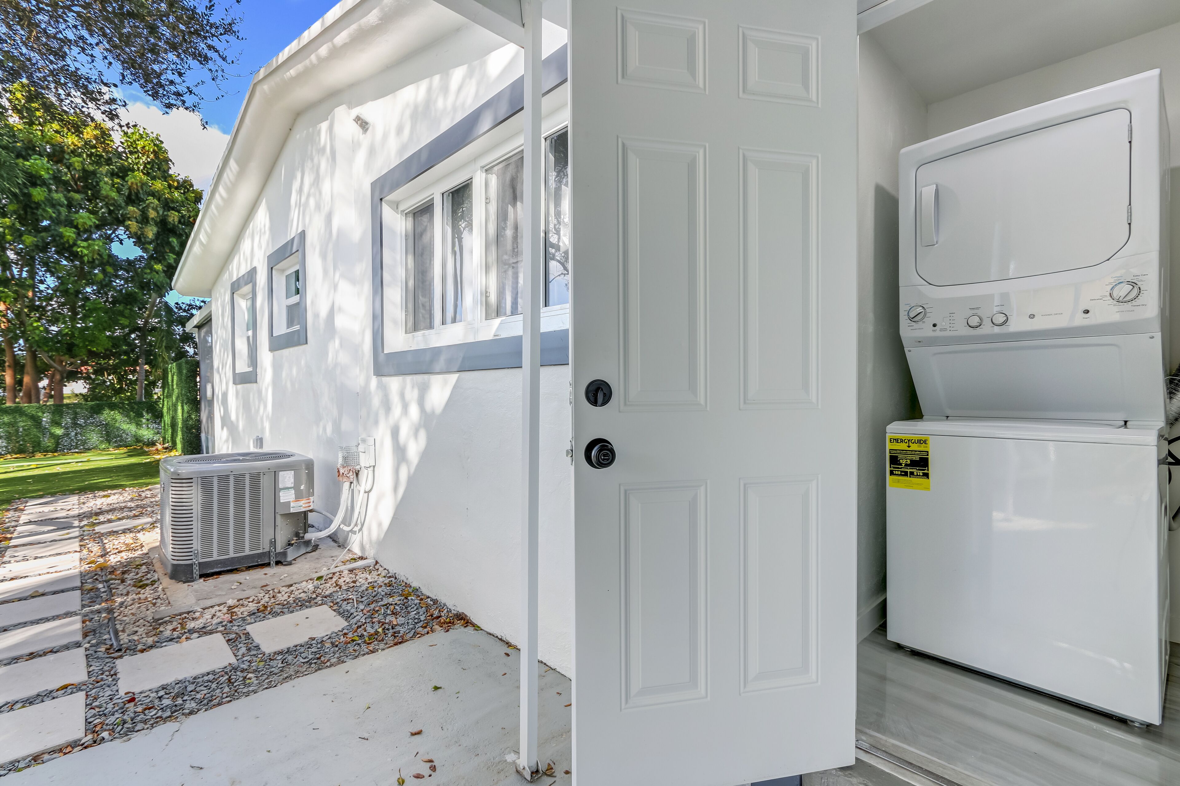 A white portable laundry unit with a control panel, a door, and an air conditioning unit outside.