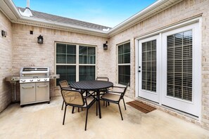 A patio with a grill, dining table, and chairs.