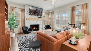 Ein modernes Wohnzimmer mit Kamin, Ledersofa und Essbereich mit Pendelleuchten.