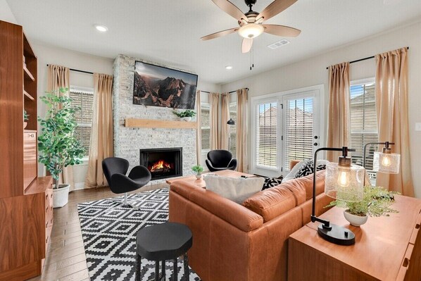 A modern living room with a fireplace, leather sofa, and a dining area with pendant lights.